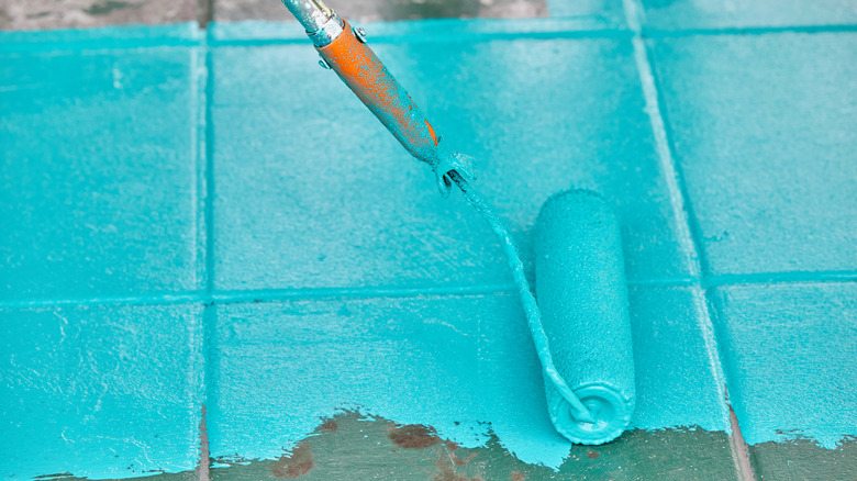 A paint roller paints old green tile a bright teal color.