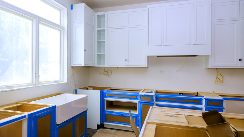 A kitchen mid-renovation with the cabinets removed and lined with blue painter's tape