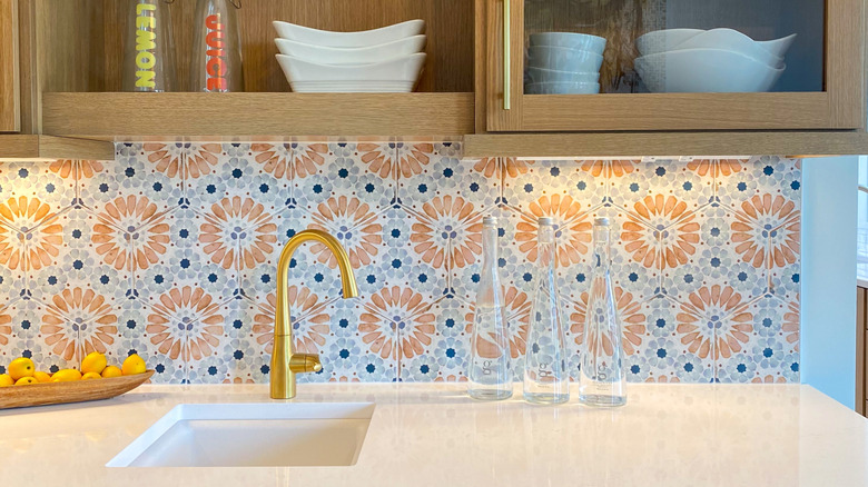 Unique floral tile backsplash with light wood cabinets.