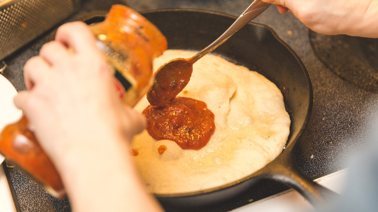 Person pouring tomato sauce on top of skillet pan pizza dough