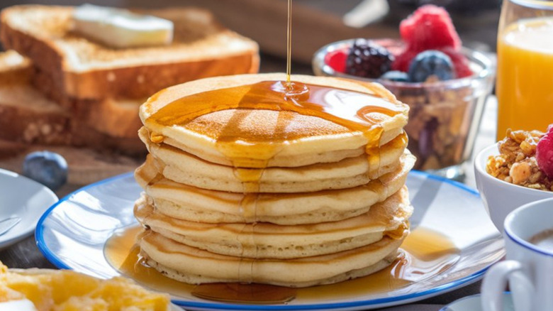 Stack of pancakes surrounded by ingredients like fruit and granola