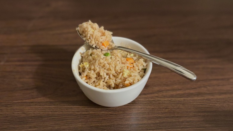 Small white bowl of fried rice with silver spoon full of rice resting on top