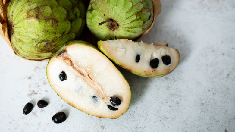 Pawpaw fruits sliced open and whole on a gray background.