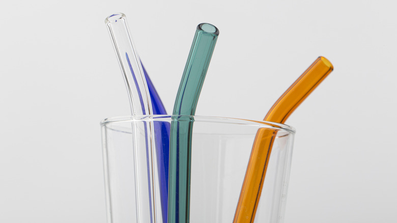 Glass of colorful, eco-friendly reusable glass drinking straws against a white background