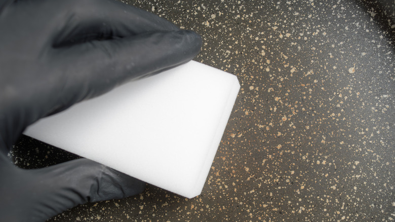A gloved hand cleans a nonstick pan with a soft, non-abrasive sponge