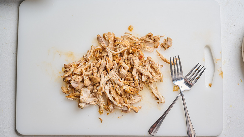 shredding chicken on a cutting board