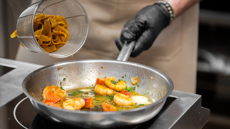 chef adds cooked pasta to saucier pan with shrimp sauce