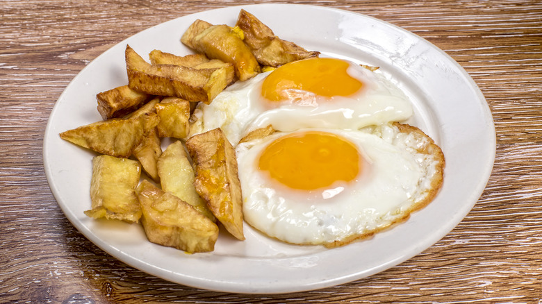White plate with egg and chips on a wooden table