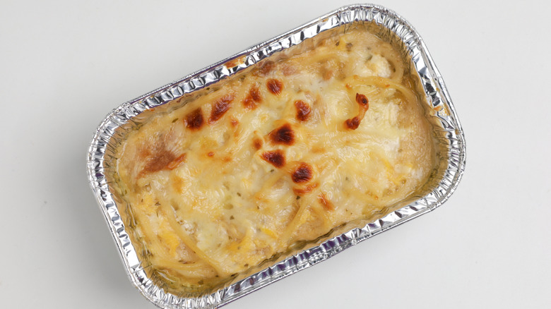 Baked macaroni pasta with a cheesy sauce in an aluminum dish on a white background