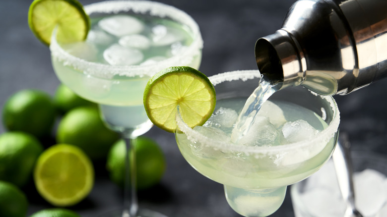 Two margarita cocktails with salt and lime slices around the rim of the glasses