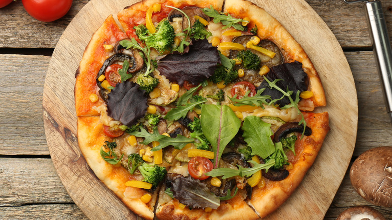Vegetarian pizza surrounded by ingredients on a wooden table