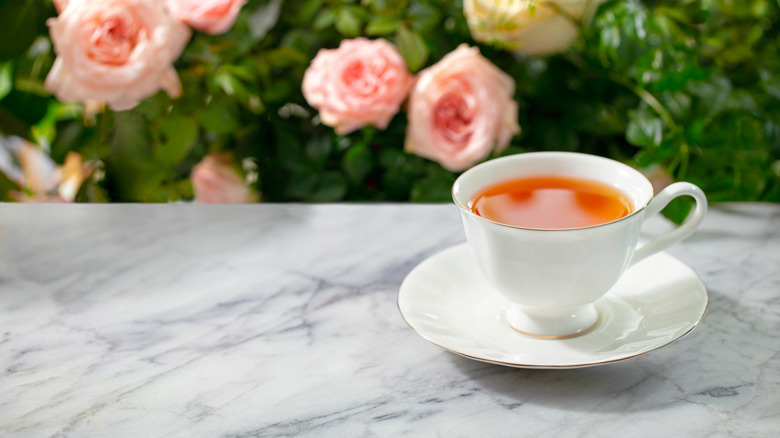 Teacup with tea on a marble table with a rose bush in the background