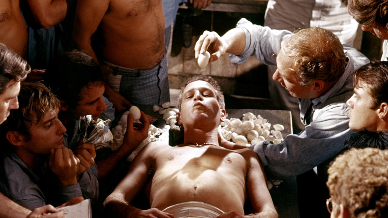Paul Newman in the movie Cool Hand Luke with hard boiled eggs arranged in front of him and someone peeling one to the right