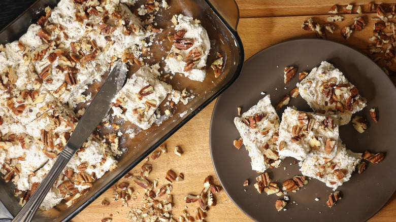Glass baking dish and brown plate full of slices of divinity white candy topped with chopped pecans with slices on plate