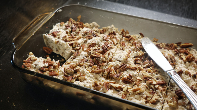 Glass baking dish and brown plate full of slices of divinity white candy topped with chopped pecans