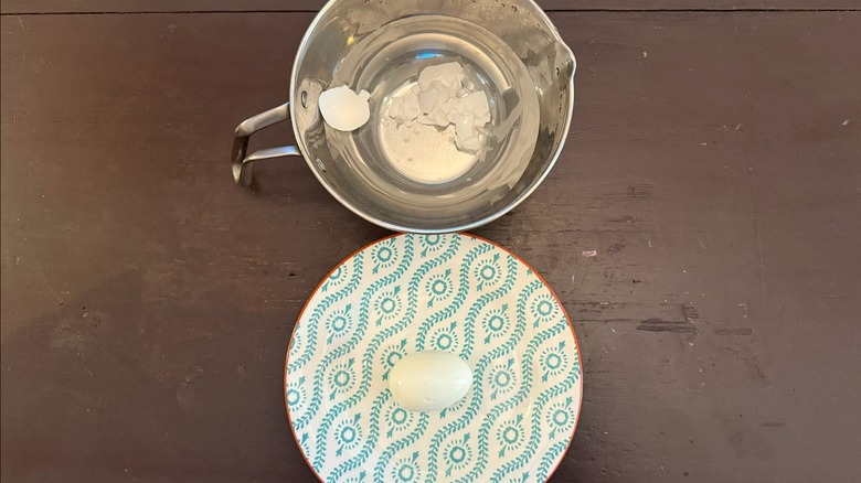 a bowl with water and shells and a freshly peeled hard-boiled egg