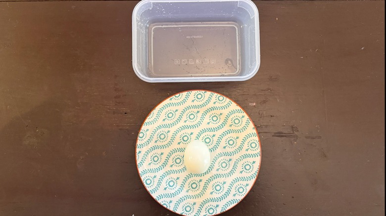 an open container and a peeled hard-boiled egg on a plate