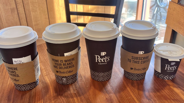 Close view of several Peet's hot drinks on a wooden table in front of a window