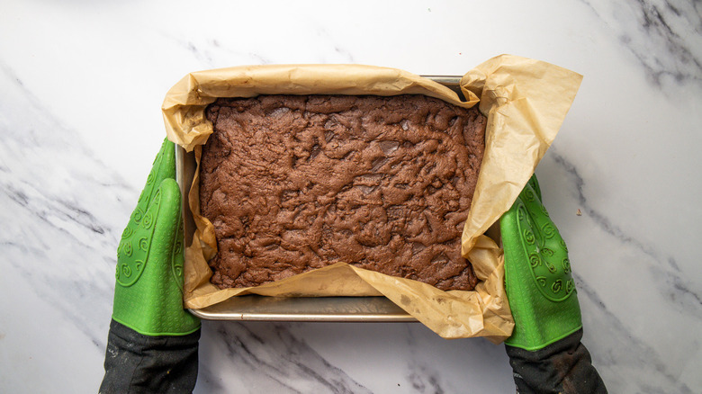 Hands serving a baked chocolate brownie base