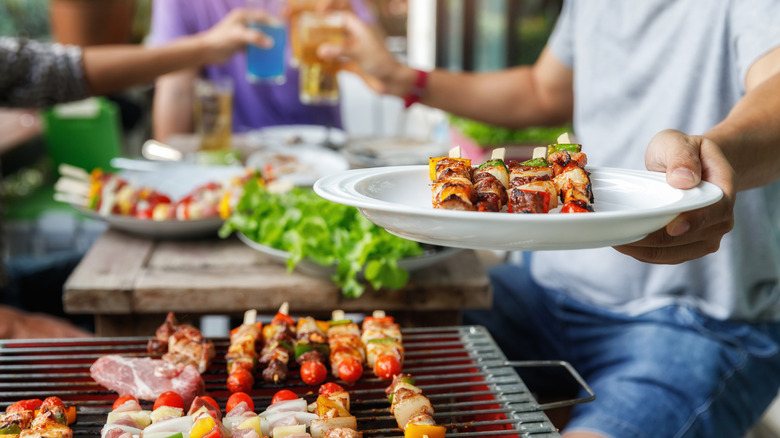 a man at a grill out hands a plate of food over the grill