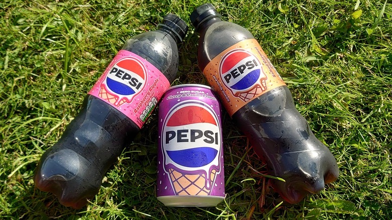 The three drinks laid out of grass, with the bottled angled into the can