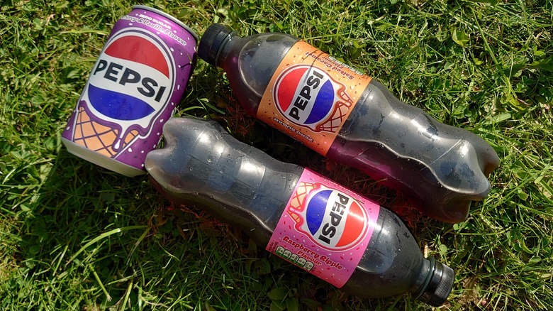 The three drinks laid out on grass, with the bottles side by side next to the can