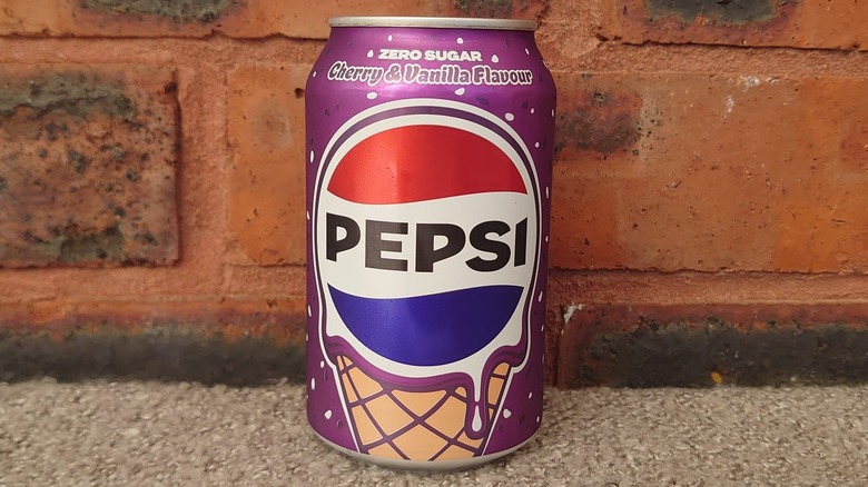 A close up shot of a Pepsi Cherry & Vanilla can on a blanket and a red brick background