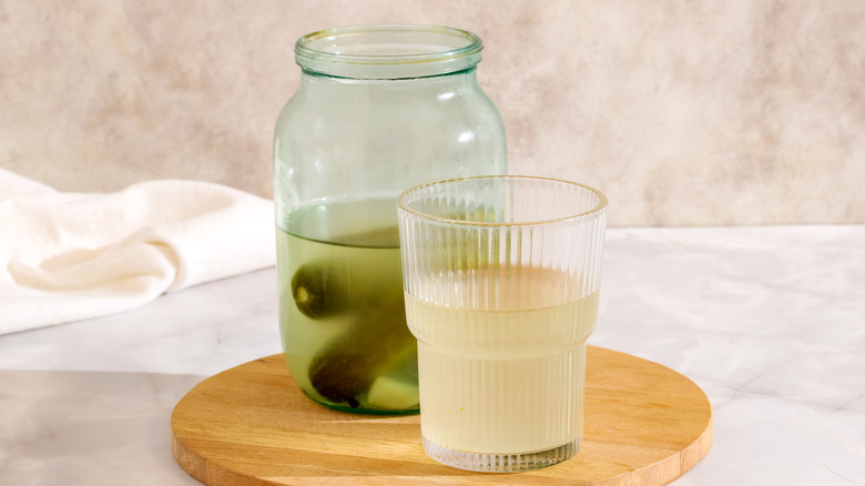 pickle juice in a glass alongside a jar of pickles
