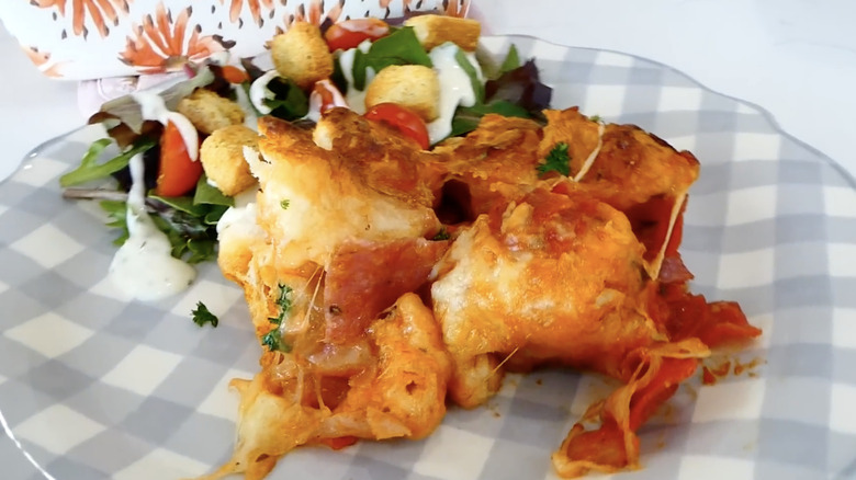 a slice of Italian sub-style casserole on a plate accompanied by a side salad