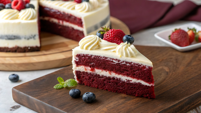 slice of red velvet cake cut from whole cake with berries and icing