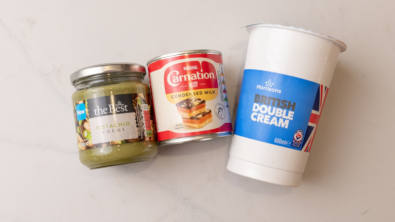Jar of pistachio creme, can of condensed milk, and British double cream laid out on marble surface