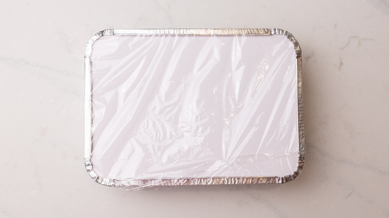 ice cream mixture in foil container wrapped with food wrap on marble surface