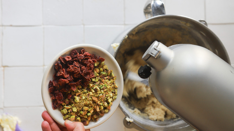 A stand mixer with a bowl of dried cranberries and chopped pistachios over it