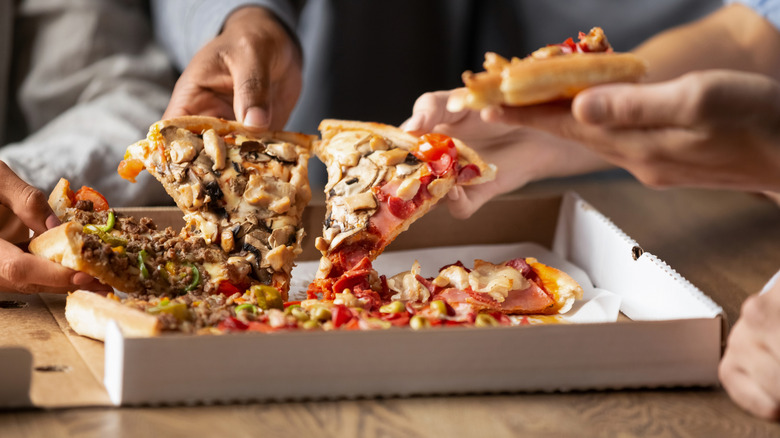 Hands reaching for slices of takeout pizza