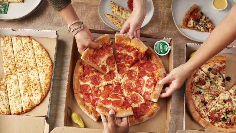 Three boxes of Papa Johns pizza on a table with hands reaching for slices of pepperoni pizza