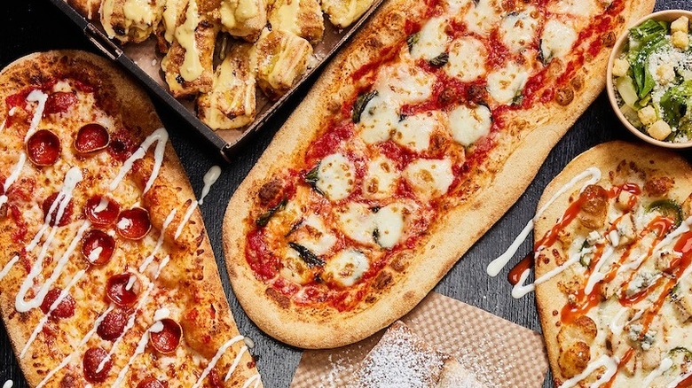 Oblong pizzas from &pizza on a table with a side salad and bread