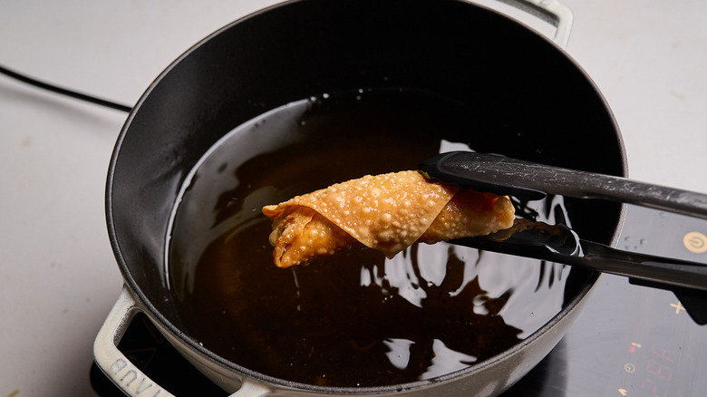 pulling egg roll out of oil with tongs