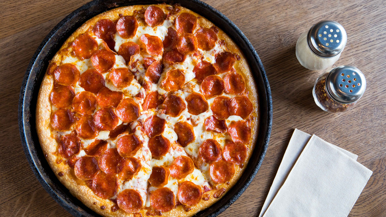 Top view of a Pepperoni pan pizza in case iron pan next to salt and pepper