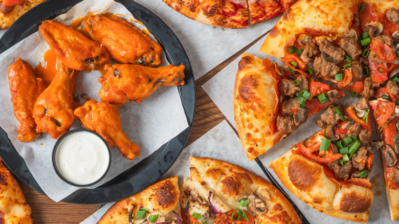 Pizza and chicken wings on a table with sauces, salads, and sides