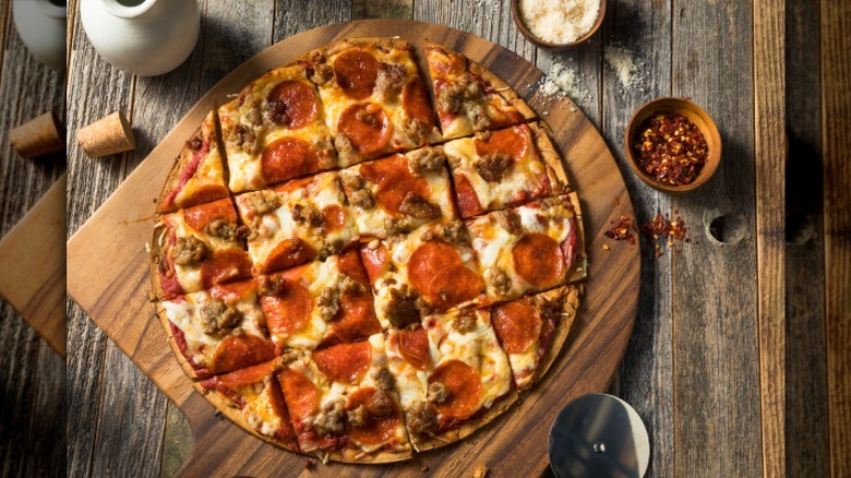 A St. Louis-style pizza sitting on a wood pizza board with chili flakes nearby.