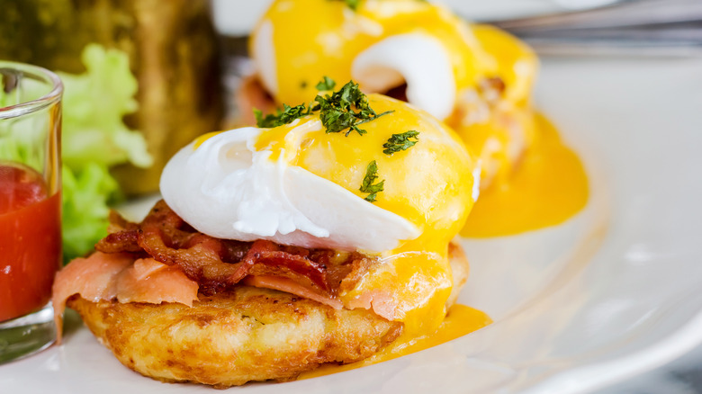 Eggs benedict with bacon sprinkled with fresh parsley served on plate with tomato juice on the side