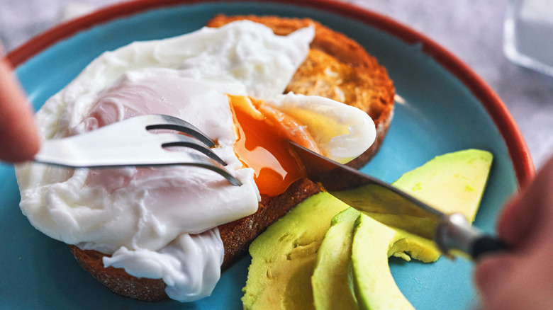 Cutting into a poached egg over toast and avocado