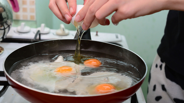 A person cracks an egg into a pan of water