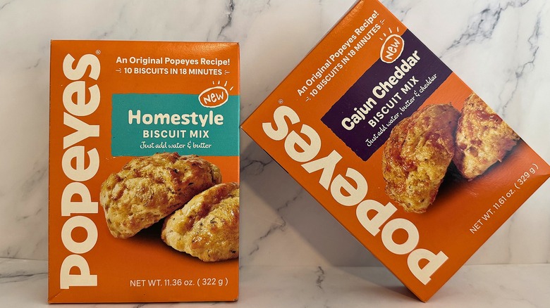 Popeyes Cajun Cheddar Biscuit Mix tilted against Popeyes Homestyle Biscuit Mix on marble background