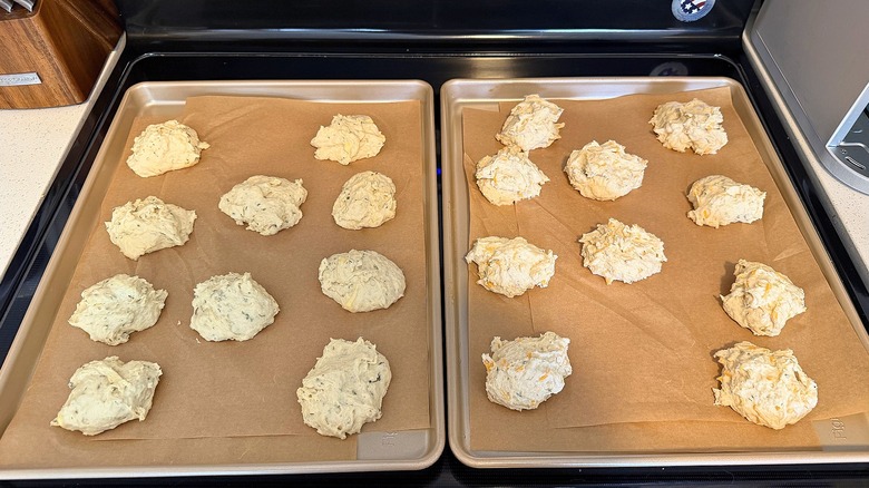 Two trays of unbaked Popeyes biscuits on parchment paper