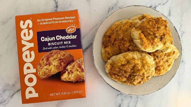 Popeyes Cajun Cheddar Biscuit Mix box next to biscuits on plate on marble surface