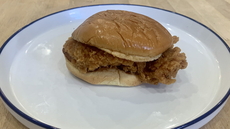 Popeyes spicy chicken sandwich on white plate with wood background