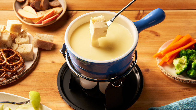 Cheese fondue in a blue pot surrounded by dipping items