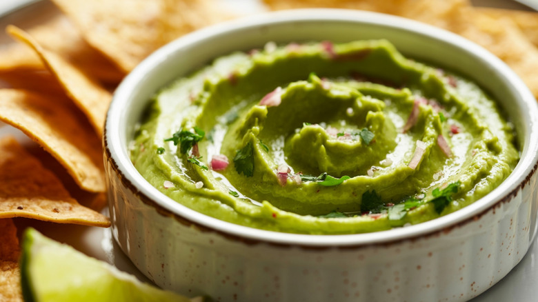 Close-up on a bowl of guacamole, with chips and lime around the edge
