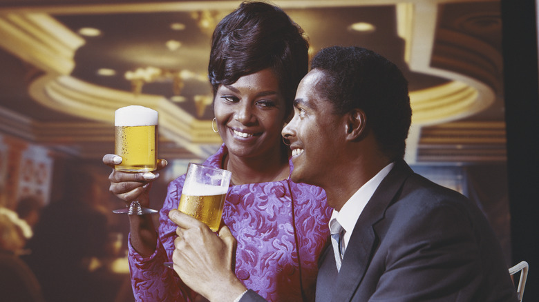 Two people holding glasses of beer and smiling at each other